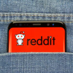 CHILLING Crackdown: Government Hunts Reddit Users… Phone displaying Reddit logo in pocket of blue jeans.