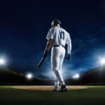 A baseball player standing on the field at night, holding a bat