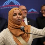 Omar’s Wealth DISAPPEARS Hours Before Ethics Deadline… Ilhan Omar speaking passionately at a podium with a group of supporters behind her