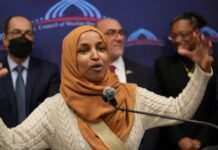 Omar’s Wealth DISAPPEARS Hours Before Ethics Deadline… Ilhan Omar speaking passionately at a podium with a group of supporters behind her