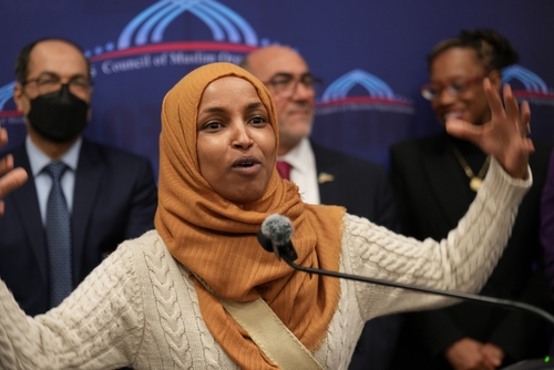 shutterstock_2622593743.jpg Ilhan Omar speaking passionately at a podium with a group of supporters behind her