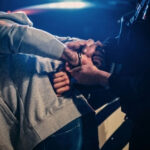 66 Charges UNLEASHED: Justice System Fumbled? Person being handcuffed by an officer beside a police car at night