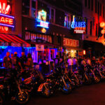 RECALL: Harley Component SNAPS — Blowout Risk Confirmed… Vibrant street scene at night with neon signs and parked motorcycles