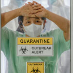 EBOLA EMERGENCY: Americans Exposed To Outbreak… A healthcare worker in a green uniform and mask, looking distressed behind a glass door marked with quarantine signs