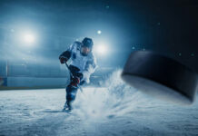 Hockey Legend Found DEAD — Furniture Store Mystery… A hockey player shooting a puck on an ice rink under bright arena lights