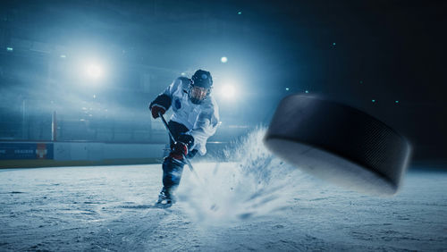 shutterstock_2018934275 A hockey player shooting a puck on an ice rink under bright arena lights