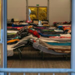 7,000 Gallon Tank CRISIS Sparks Mass Evacuations Interior view of a temporary shelter with rows of beds.