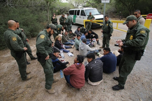 shutterstock_2268609071 Border patrol agents detaining a group of immigrants.
