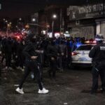 Masked Mobs Storm Brooklyn – Police SCRAMBLE… Crowd of people gathered on a street with police officers and vehicles