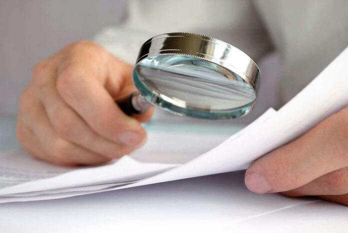 115187251 Person examining document with magnifying glass.