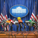 White House Memo Ends War—Or Just Hype? White House podium with multiple microphones and flags.