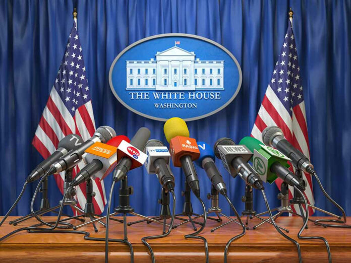 1186435138 White House podium with multiple microphones and flags.