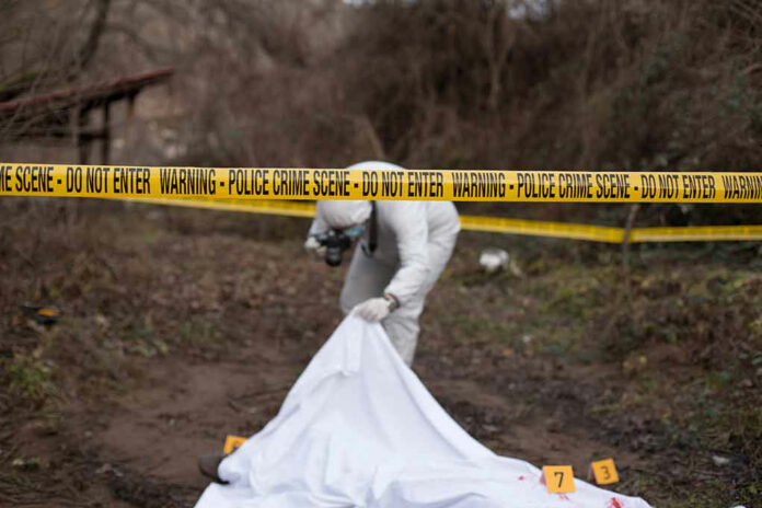 792627700 Police crime scene with investigator examining covered body