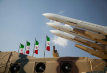 IAEA Alarm — Iran Closes Bombed Sites Missiles on launchers beside Iranian flags.