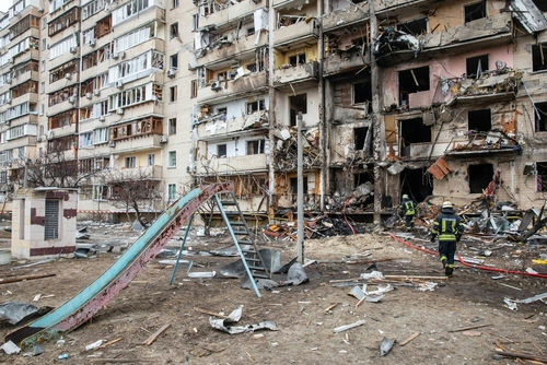 shutterstock_2129012939 Damaged apartment building with debris scattered firefighters present.