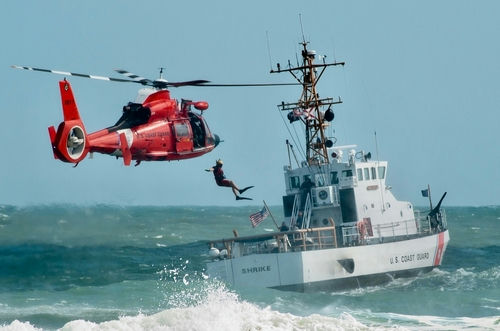 shutterstock_2307202521 Coast Guard training with helicopter and boat in rough seas.