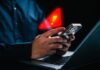 Person holding a smartphone with a notification alert while using a laptop