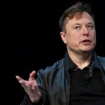 A man in a black leather jacket speaking at a conference