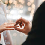 Reality ‘Healing’ Sells While Marriages Sink Groom placing ring on brides finger at wedding.
