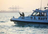 U.S. Navy patrol boat on water near industrial port.