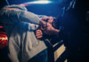 Person being handcuffed by an officer beside a police car at night