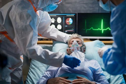 shutterstock_1661222104 Patient on hospital bed with oxygen mask assisted by healthcare workers
