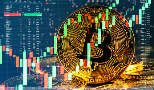 shutterstock_1888907947 Bitcoin symbol overlaid with stock market graphs.