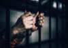 Hands gripping prison bars, suggesting confinement