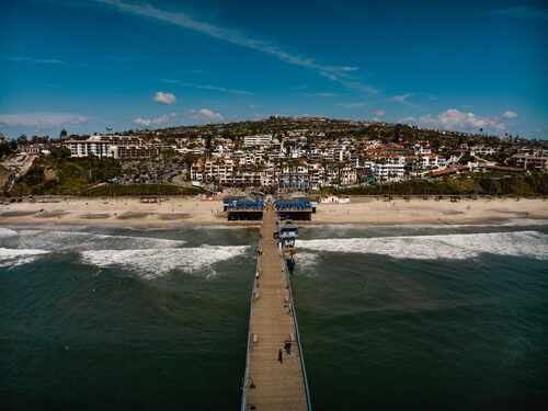 April,2024,,San,Clemente,,Ca,-,Drone,View,Of,San Aerial view of a pier extending into the ocean with a beach and residential area in the background