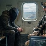 Pentagon Power Play Halts Safety Probe A hooded figure sits quietly in a helicopter with soldiers, overlooking a city skyline.