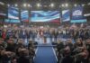 A political convention with speakers on stage and a cheering crowd holding signs and flags