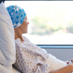 Stunning Switch: Midlife Moms Overtake Teens A female patient in a hospital bed wearing a blue patterned headscarf, looking out a window