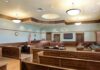 Empty courtroom with wooden benches and desks.