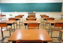 Empty classroom with wooden desks and chalkboard.