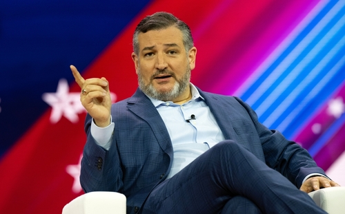 A man speaks at a conference, gesturing with his hand.