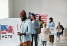 People voting at polling station with American flag nearby.