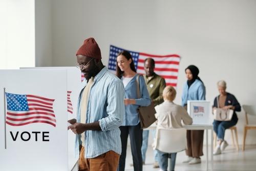 People voting at polling station with American flag nearby.