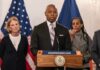 People standing at a podium with flags behind them.